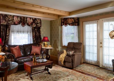 Crown Jewel Sitting Room with Leather Sofa, Reclining Chair and Wine Glasses on the Coffee Table. Double French Doors on the Right.