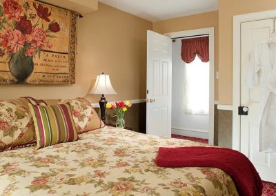 Close-up photo of the Brighton Bed, detailing the beautiful golds, greens and burgundy in the bedding and the floral tapestry above the bed