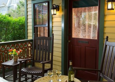 Close-up photo of the Regent's Park porch with two rocking chairs and a yellow wicker table with a bottle of white wine and two filled wine glasses.