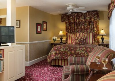 Whitehall guestroom with queen bed with coordinating burgundy floral fabric quarter canopy, Two striped comfy chairs